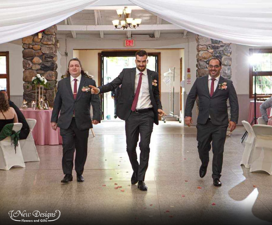 3 groomsmen walk into the reception hall sporting pocket square floral installments in shades of white and pink